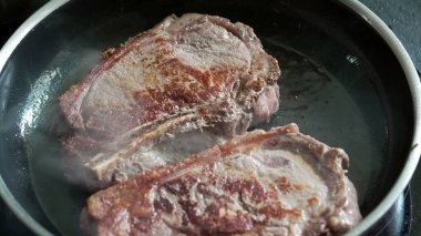 Sıcak tavada pişen biftekler, kahverengileşmeye başlıyor, taze sığır eti, cızırtılı ses, ev mutfağı, mutfak hazırlığı, lezzetli bir yemek hazırlama, pişirme sürecinin detaylı görüntüsü.