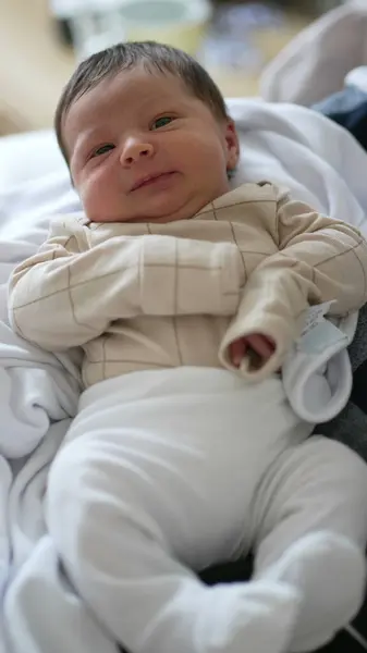 stock image Newborn baby in a beige outfit, resting comfortably on a soft blanket, curious and calm expression, a peaceful moment of early life in a home environment