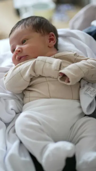 stock image Newborn baby in a beige outfit, resting comfortably on a soft blanket, curious and calm expression, a peaceful moment of early life in a home environment