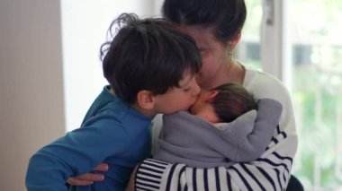 Büyük oğlan hem anne hem de yeni doğmuş bebeği öpüyor, sevgi ve bağla dolu şefkatli ve yürek ısıtan bir aile anı yaratıyor, anne ve kardeş arasındaki bağı vurguluyor.