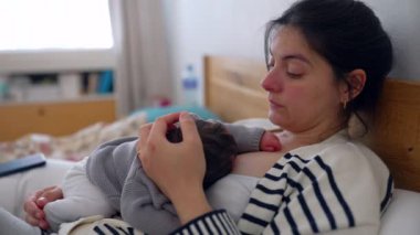 Anne, uyuyan bebeği göğsünde yatağında dinlenirken, gözleri bir an için sessiz bir yansımayla kapanıyor. Anne ve bebek arasında paylaşılan huzur ve huzur.