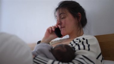 Anne, bebeği kollarında huzur içinde uyurken telefonda düşünceli bir ifadeyle konuşurken birden fazla iş yapıyor. Uyuyan bir bebeğe bakmakla günlük sorumluluklarını yerine getirmek arasındaki denge.