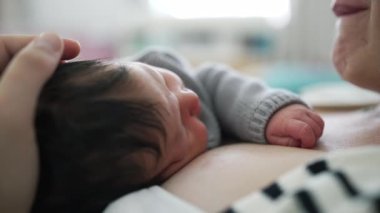 Anne, bebek göğsünde uyurken bebeğin başını nazikçe sarkıtıyor. Yumuşak bir bağ kurma ve rahatlama anı yaşıyor. samimi bağlantı ve bakım