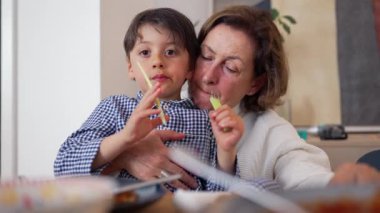 Büyükannem yemek masasında küçük bir çocuğu besliyor, sıcak bir ev ortamında paylaşılan bir yemek sırasında nesiller arasında hassas ve besleyici bir anı gösteriyor.