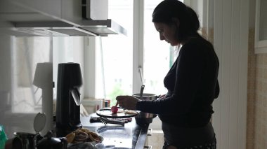 Mutfakta pembe spatula kullanan bir kadın. Görüntü, sıcak bir ev mutfağında tipik bir günü gösteren bir yemek hazırlarken gösterilen özverinin ve konsantrasyonun altını çiziyor.