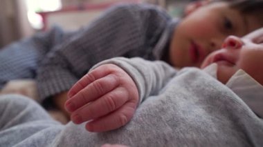 Arka planda ağabeyi olan yeni doğmuş bir bebeğin el ve yüzüne yakın plan, huzurlu bir yuvadaki kardeşler arasındaki hassas ve nazik dokunuşu yakalıyor.
