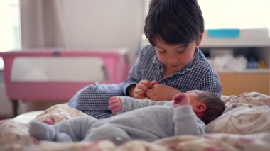 Ağabeyi, yeni doğan kardeşe yakın duruyor. Yatakta şefkatli bir anı paylaşırken sıcak bir şekilde gülümsüyor. Sevgi dolu bir ailede büyüyen sevgi ve bağlarını vurguluyor.