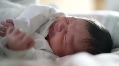 Yeni doğan bebek uykusunda yüzünü buruşturuyor, rahatsız edici bir görüntü sergiliyor, muhtemelen gaz çıkarıyor, erken yaşların doğal ve samimi anlarını yakalıyor.