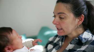 Bir anne tarafından tutulan yeni doğmuş bir bebeğin yakın plan çekimi. İkisi de yumuşak ifadelerle birbirlerine bakıyor. Samimi ve sakin iç mekan ortamları.