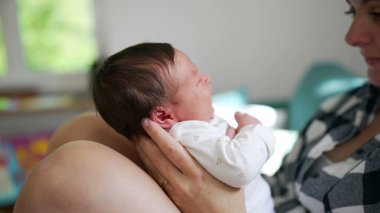 Bir anne tarafından tutulan yeni doğmuş bir bebeğin yakın plan çekimi. İkisi de yumuşak ifadelerle birbirlerine bakıyor. Samimi ve sakin iç mekan ortamları.