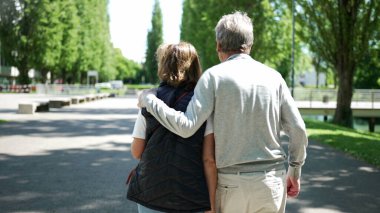 Yaşlı çift parkta kol kola yürüyor, arkadan bakıyor, güneşli havanın tadını çıkarıyor, yeşillik, son sınıf aşkı ve arkadaşlıkla çevrili, boş zaman, barışçıl ve sevgi dolu bir ilişki.