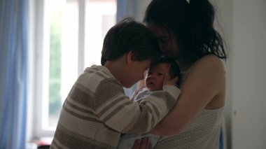 Ağabeyi yeni doğan kardeşine nazikçe dokunurken, annesi onları kucağında tutuyor, hassas bir aile bağını ve yeni bir aile üyesini ağırlamanın sevincini vurguluyor.