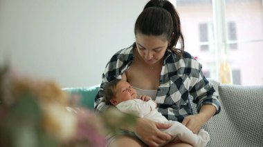 Anne bebeğini emzirmek üzere, kendini yeni doğan bebeğine süt vermeye hazırlıyor, rahat bir ev ortamında, rahat bir kanepede oturuyor, güçlü bir sevgi, ilgi ve annelik duygusu var.