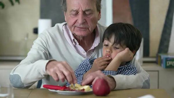 Stock image Grandfather guiding his young grandson in slicing an apple, emphasizing the bond between generations, teaching, and sharing valuable life skills in a cozy, home environment, featuring close family ties