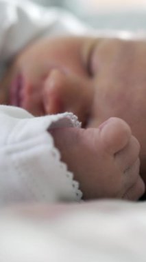 Yeni doğmuş bir bebeğin huzur içinde uyuduğu yakın plan, odak noktasında narin yüz hatları, yumuşak battaniyeler, sıcak ve rahatlatıcı atmosfer ile çevrili huzurlu ve sessiz bir dinlenme anı yakalıyor.