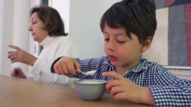 Yemek masasında yoğurdun tadını çıkaran genç bir çocuk evde sakin bir yemek yerken, çocukluğun basit zevklerini vurguluyor.