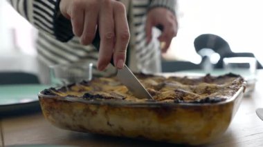 Elle pişirilmiş bir tabağı kesmek, aile yemeklerinin ev yapımı konforunu sergilemek, geleneği, sıcaklığı ve rahat bir evde yemek masasının etrafında paylaşılan anları vurgulamak.