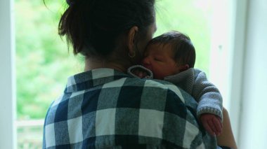 Yeni doğan bebek annesinin omzunda dinleniyor, sevgi dolu bir kucaklaşmanın sıcaklığını ve güvenliğini yakalıyor.