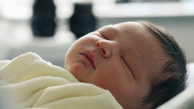 Yeni doğmuş bebek, yumuşak sarı bir battaniyeye sarılı huzurlu bir ifadeyle uyuyor. Yeni doğan hayatın masumiyetini ve sükunetini vurgulayan hassas özellikler.