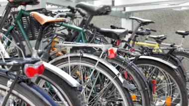 Park halindeki bisikletlerin yakın çekimleri. Lastiklerin, eyerlerin ve arka farların detaylarına odaklanıyorlar. Kentsel bir ortamda bisikletlerin günlük kullanımı ve tasarımı