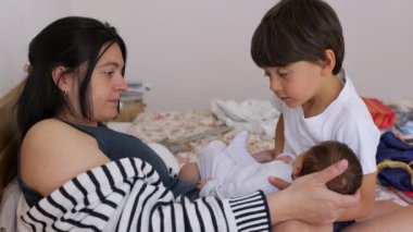 Anne ve ağabeyi yeni doğmuş bebeği bir arada tutuyor, sıcak aile bağı, bakım, şefkatli kardeş bağı, rahat ev, erken çocukluk aşkı, huzurlu ev ortamları, doğal ışık.