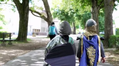 Şövalye gibi giyinmiş iki çocuğun, bir sonraki yaratıcı maceralarına doğru parka doğru yürüyüşlerinin arka görüntüsü. çocukluğun neşeli ruhu ve merakı
