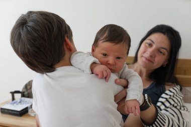 Yenidoğan bebek, ağabeyi tarafından tutuluyor ve annesi tarafından izleniyor. Aile bağları ve aile sevgisinin hassas bir anını yakalıyor. Aile ve çocukluk teması için mükemmel.