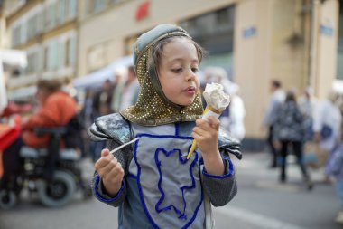 Ortaçağ şövalyesi kostümü giymiş bir çocuk açık hava festivalinde dondurma külahının tadını çıkarıyor. Eğlenceli sahne, tarihi canlandırma ile günlük eğlenceyi birleştirir. Çocuğun zevkini gözler önüne serer.