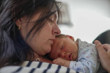 Anne bebeğini kucağında tutuyor, ikisi de kanepede huzur içinde uyuyor, güçlü bir annelik bağı kuruyor ve evlerinde bir anlık huzur yaşıyor.