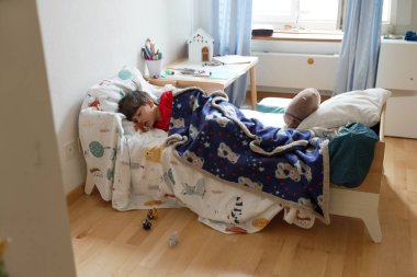 Young boy sleeping soundly on his bed, wearing a red shirt and resting on animal-themed sheets, encapsulating a peaceful and serene childhood moment of rest and comfort clipart