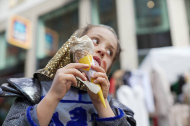 Ortaçağ şövalyesi kostümü giymiş bir çocuk açık hava festivalinde dondurma külahının tadını çıkarıyor. Eğlenceli sahne, tarihi canlandırma ile günlük eğlenceyi birleştirir. Çocuğun zevkini gözler önüne serer.