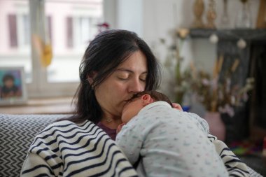 Anne uyumakta olan bebeğini nazikçe kucaklıyor. Huzurlu bir anda derin bir sevgi ve ilgi gösteriyor. İkisi de rahat ve rahat. Yakın bir aile bağını vurguluyorlar..
