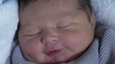 Yeni doğmuş bir bebeğin yüzünün yakın çekimi, uykusunda gözleri kapalı, huzur içindeki huzurlu bir bebeğin nazik ve narin özelliklerini vurguluyor.