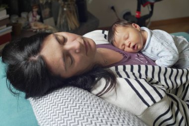 Anne bebeğini kucağında tutuyor, ikisi de kanepede huzur içinde uyuyor, güçlü bir annelik bağı kuruyor ve evlerinde bir anlık huzur yaşıyor.