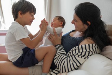 Küçük çocuk yeni doğan kardeşiyle etkileşime geçiyor, iç açıcı bir aile anı yaratıyor, kardeş sevgisini, aile bağını ve çocukluk neşesini ön plana çıkaran görseller için ideal