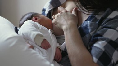 Anne, beyaz giysilere sarılı olarak yeni doğan bebekleri emziriyor, anne bakımını ve yakın ilişki anlarını gösteriyor, erken çocukluk gelişiminde emzirme ve beslemenin önemini vurguluyor.