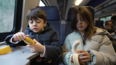 Trende muz yiyen iki çocuk, yan yana seyahat ederken basit bir atıştırma anı yakalıyorlar, çocukluğu, beslenmeyi ve tren yolculuğunun neşesini vurguluyorlar.