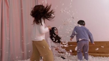 Çocuklarla Yastık Dövüşü Sahnesi ve Pembe Perdeli Bir Odada Anne, Pembe Tüyler Uçuyor, Neşeli ve Enerjik Bir Aile Anı Oluşturuyor, Eğlenceli ve Birlikte Olmayı Vurguluyor