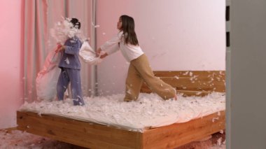 Oğlan ve kız, yatakta tüyleriyle heyecan verici yastık kavgası yapıyor eğlenceli ve keyifli bir anda etrafta uçuyor çocuklar rahat pijamalarıyla gülüyor ve oynuyorlar.