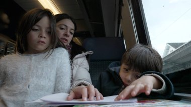 Anne ve çocuklar tren yolculuğu sırasında etkinlik göstererek aile bağı kurma ve toplu taşımada öğrenme anlarını yakalıyorlar.
