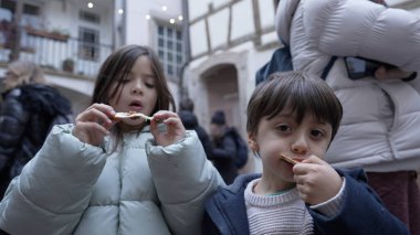 Şehir caddesinde pizza yiyen, kışlık ceket giyen, yemek yiyen, şehir manzarasının tadını çıkaran, çocukluk sevincini ve sokak yemeği kültürünü yakalayan, kardeşlerin eğlenceli bir anı paylaşması,