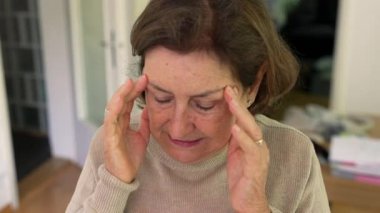 Olgun bir kadın yoğun bir baş ağrısı ya da stres yaşıyor, iki eliyle başını tutuyor, rahatsızlık ve endişelerini dile getiriyor. Yüz kırışıklıkları ve konsantrasyon, fiziksel ya da duygusal acı