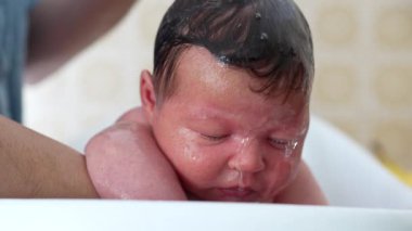 Yeni doğmuş bebek banyo zamanı içerikli bir ifadeyle, ebeveynin elinden desteklenerek, sıcak ve besleyici bir ortamda sevgi ve şefkati gösteriyor.
