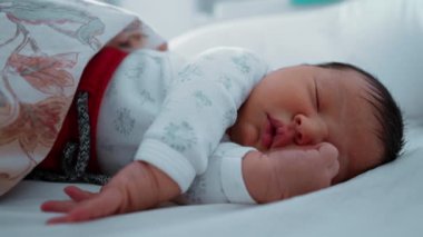 Yeni doğmuş bebek yatakta huzur içinde uyuyor, kısmen desenli bir battaniyeyle örtülü. Yavruların sakin ifadeleri ve rahat çevreleri bir huzur ve sükunet anı yakalar. 