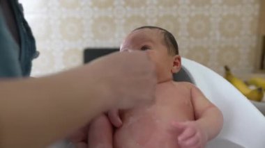 Yeni doğan bebek, küçük bir küvette nazikçe banyo yapıyor, kafalarından aşağı su dökülüyor, yüz ifadelerinin ve deri dokusunun yakından görüntüsü.