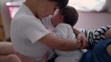 Ağabeyi bebeği nazikçe kucağına alıyor, sıcak aile bağı, yakın bağ kurma anı, yetiştirme bakımı, evde rahat bir ortam, kardeş sevgisi, erken çocukluk, doğal ışık.