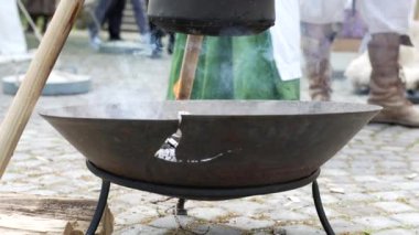 Bir canlandırma etkinliğinde bir kazanın üzerine kazan konmuş bir ortaçağ yemek setinin yakın çekimi, kırsal atmosferi ve geleneksel açık hava yemek pişirme yöntemlerini yakalıyor.