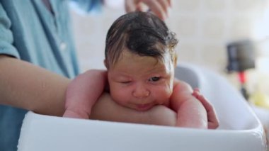 Yeni doğan bebek nazikçe banyo yapıyor, ebeveynlerinin sevgi dolu ellerine odaklanıyor, erken çocukluk hijyeninin hassas ve samimi anlarını vurguluyor.