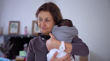 Büyükannem yeni doğmuş bir bebeği omzunda tutuyor. Mutlu ve koruyucu görünüyor. Ailevi bir sevgi ve yakınlık gösteriyor.