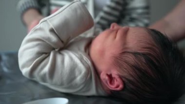 Yeni doğan bebek değişen bir paspasın üzerinde yatıyor. Anne bebek kıyafetlerini düzeltirken rahatsızlık ve şikayet belirtileri gösteriyor.